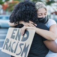 African american and caucasian females embrace, one hold and "end racism" sign.